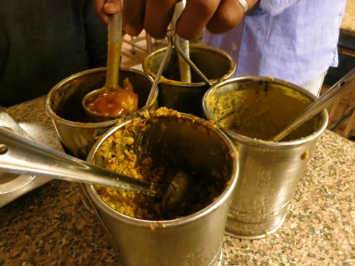 A quartet of spicy dishes being served tableside, canteen-style, at a Hydrabad restaurant